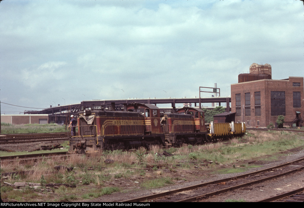 BM 1230 & BM 802 haul welded rail for the MBTA Green Line 'D' Branch past Boston Engine Terminal